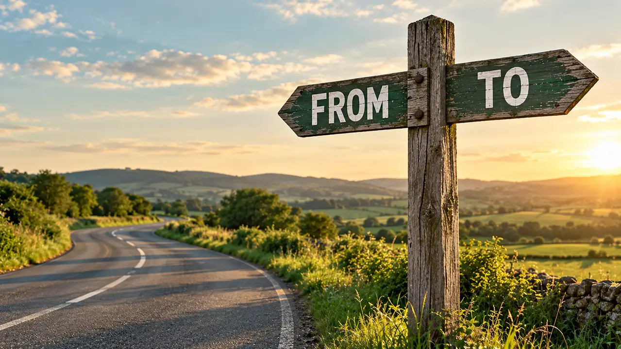 Wooden signpost on a quiet country road with one arm reading FROM pointing back and one reading TO pointing forward