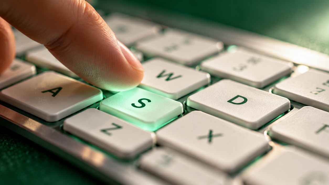 Macro view of a laptop keyboard with a fingertip pressing the glowing S key while the neighboring keys blur out